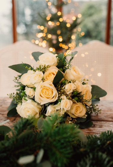 A cream rose bridal bouquet on a rustic table, with a lit Christmas tree glowing behind