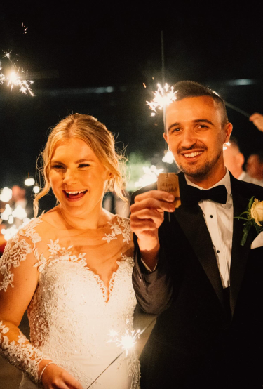 The newlyweds laughing as sparklers glow around them