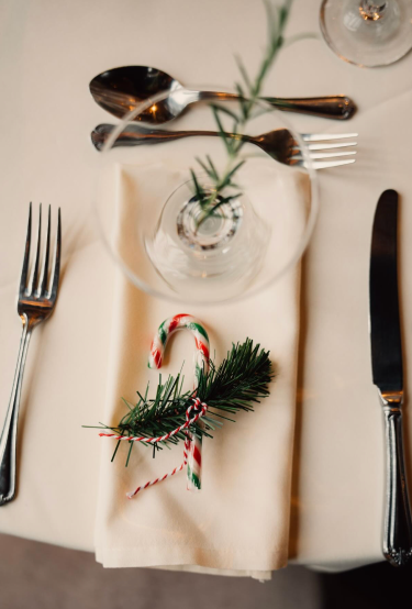 A Christmas place setting with a candy cane tied to a sprig of pine on a cream napkin
