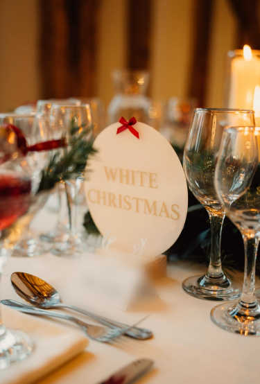 A &ldquo;White Christmas&rdquo; table sign with a red bow beside glassware