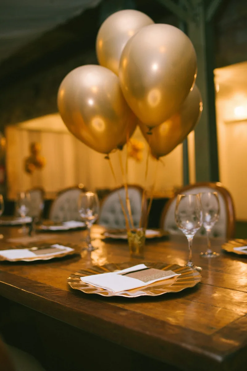 Gold balloons above a wooden table laid for a birthday dinner