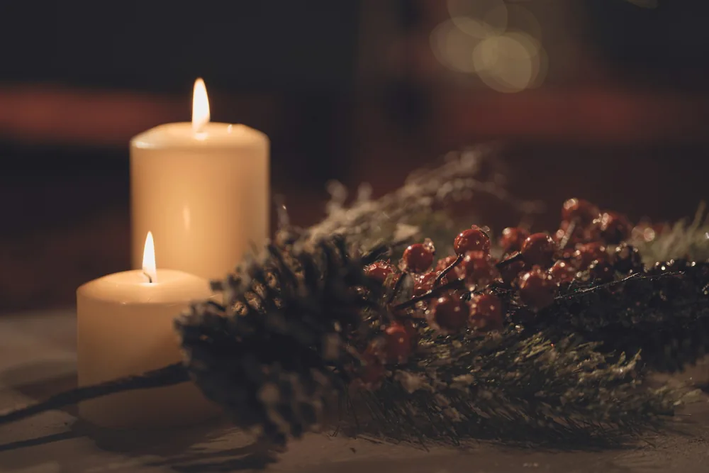 Pillar candles glowing beside a festive garland of pine and berries