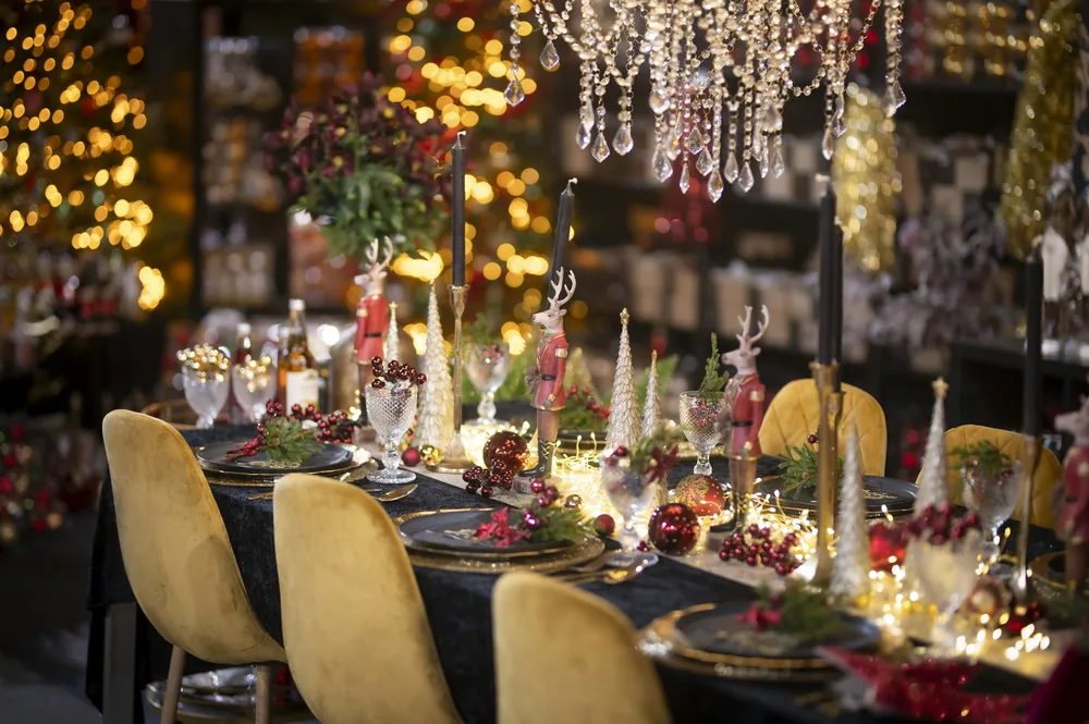 A festive dinner table glowing with candles, greenery and golden chairs