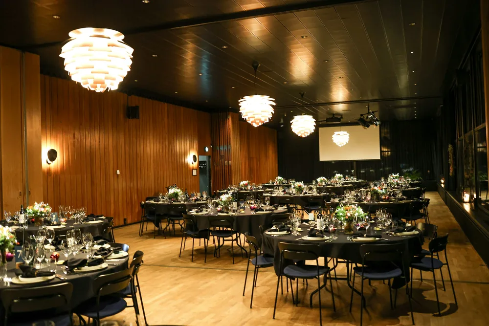 A warmly lit event room set with round dinner tables