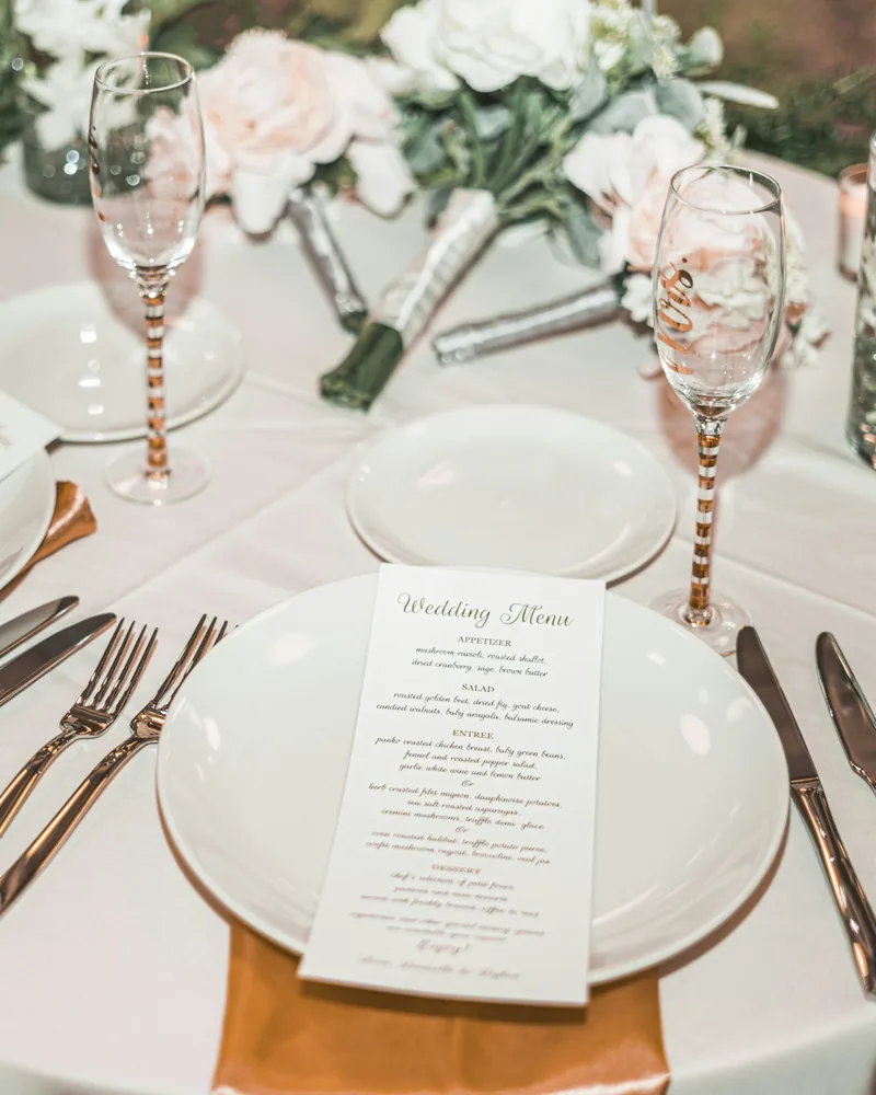 A wedding place setting with a printed menu, gold-stemmed glasses and blush flowers