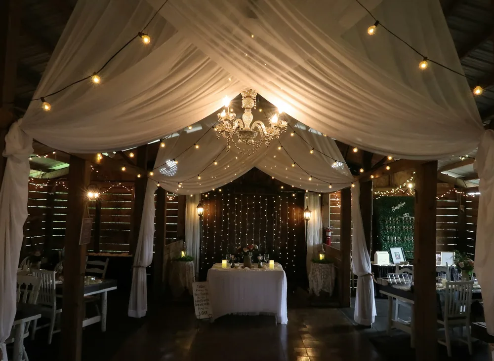 A barn wedding reception dressed with draped ivory fabric and warm lights